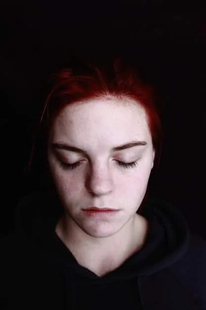 A close-up of a person's face, with a slightly downcast expression, suggesting feelings of loneliness and introspection. The lighting is soft and diffused, adding to the emotional depth of the image.