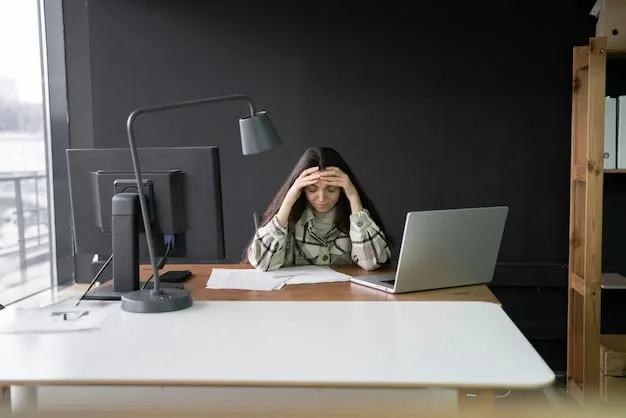 A stressed employee sitting at their desk in a modern office, with their head in their hands. The desk is cluttered with papers and a laptop. The scene conveys a feeling of overwhelm and pressure.
