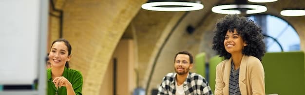 A group of people smiling and collaborating in a bright, modern office space. The focus is on their teamwork and positive energy.