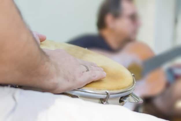 A close-up photo of a music therapist gently guiding a patient's hands as they play a drum, focusing on the collaborative and supportive aspect of the therapy session.