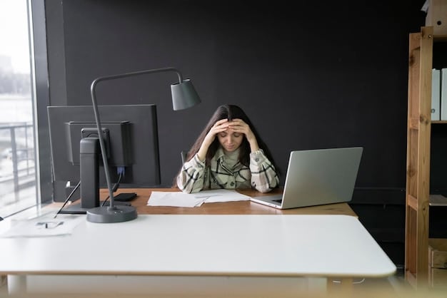 A stressed employee sitting at their desk in a modern office, with their head in their hands. The desk is cluttered with papers and a laptop. The scene conveys a feeling of overwhelm and pressure.