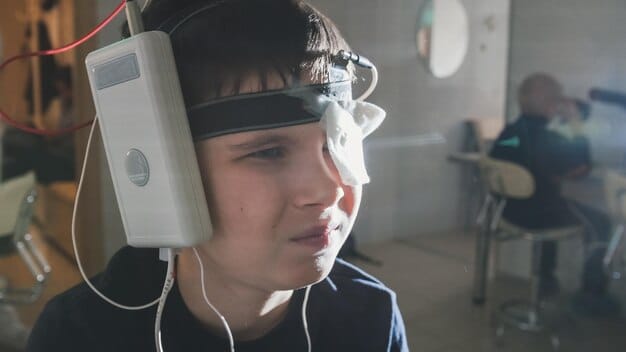 A person using EMG biofeedback, with sensors attached to their forehead and a screen displaying muscle tension levels.